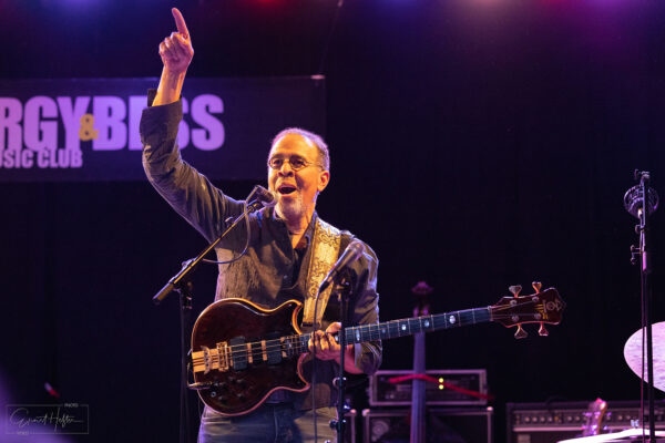 Jazz-Bassist Stanley Clarke auf der Bühne des Porgy & Bess in Wien, mit erhobenem Arm und E-Bass vor violettem Konzertlicht.